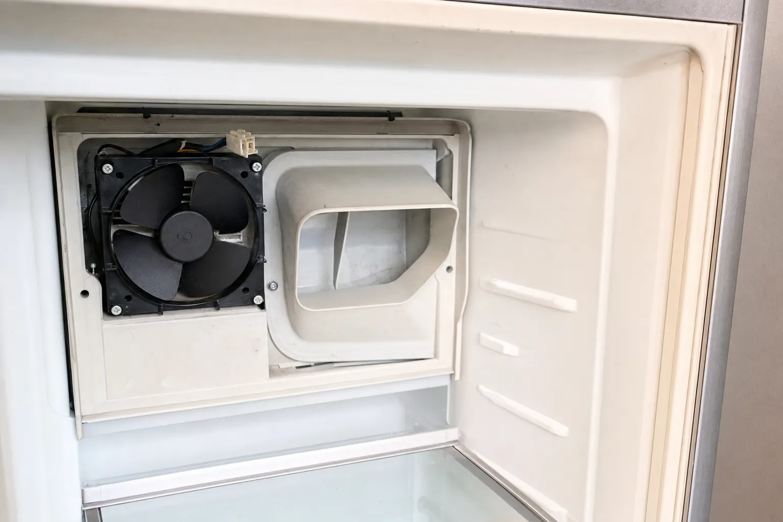 Evaporator fan and air duct exposed behind the open rear panel inside an empty freezer compartment