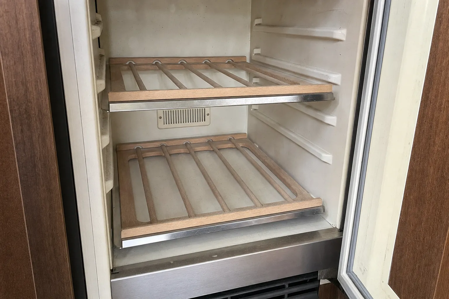 Empty undercounter refrigeration cabinet with two wooden slat shelves and a vent in the rear wall